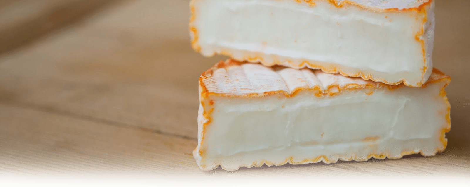 Close-up of sliced MouCo ColoRouge cheese showing its creamy interior and bold orange rind with a soft, bloomy white dusting.
