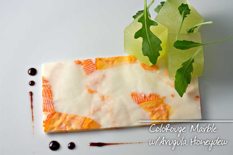 A sheet of MouCo ColoRouge cheese flattened like marble, soft and rich with bits of rind throughout. Topped with honeydew melon cubes, arugula leaves, and a drizzle of Minus 8 vinegar glaze.