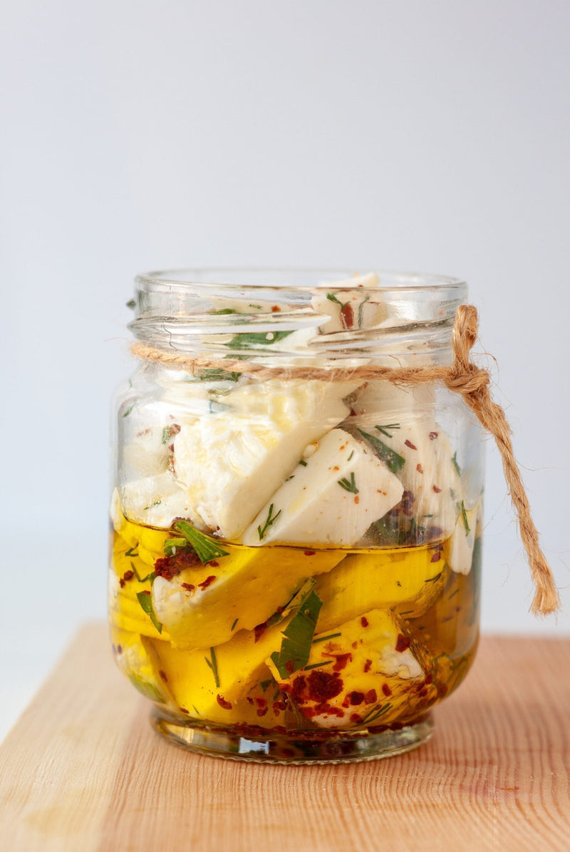 Jar of MouCo Cheese Curds marinating in olive oil with herbs and spices—Colorado-made curds ready for snacking or entertaining.