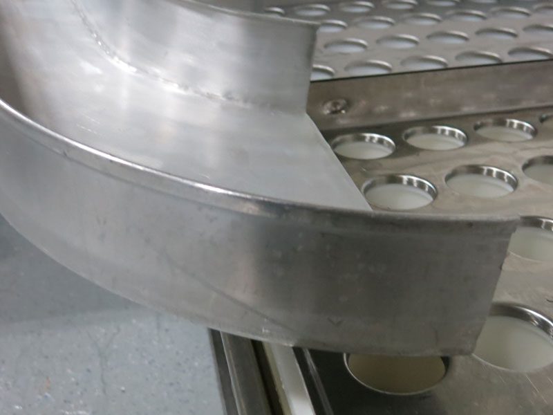 Forming: The end of the curd shoots, where curd whips around the bend into the filling funnels—360 soft-ripened MouCo cheeses coming to life in one synchronized pour.
