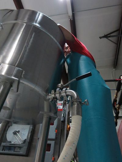 An employee overseeing the start of a MouCo cheese batch, monitoring temperature and adding ingredients as the tank fills.