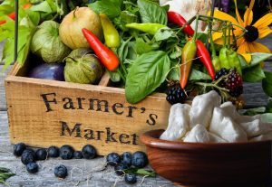 Farmers market bounty with MouCo cheese curds, peppers, spinach, flowers, blackberries, blueberries, and tomatillos in a wooden box.